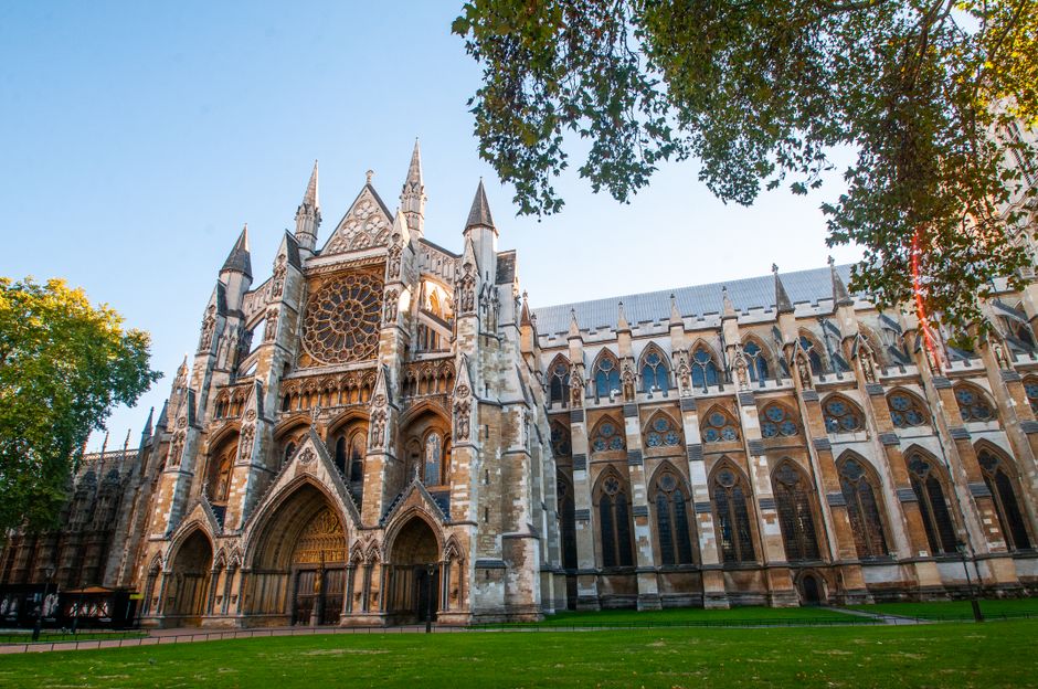 Close-up view of the exterior of a historic Gothic-style cathedral with tall, pointed spires, detailed stone carvings, large arched stained glass windows, and intricate tracery, bathed in natural dayl